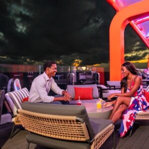 Couple enjoying romantic sunset drinks on the Magic Carpet floating deck aboard the Celebrity Beyond.