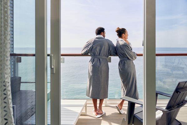 Couple in robes standing on the Infinite Veranda balcony of a Celebrity Beyond stateroom overlooking the ocean.
