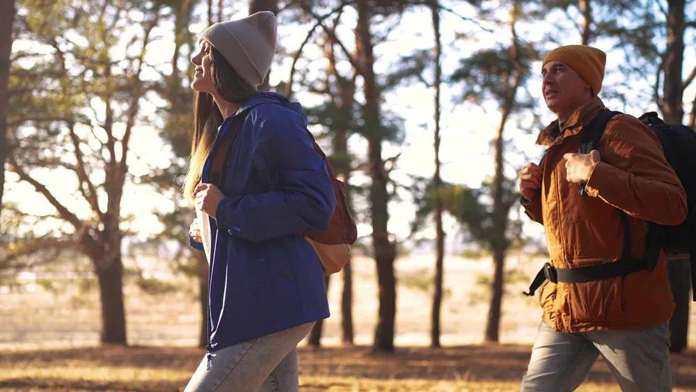 A couple hiking together through a sunlit Alaska forest with backpacks