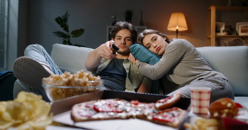 A married couple sitting disengaged on the couch at night, the quiet drift a marriage enrichment retreat helps repair