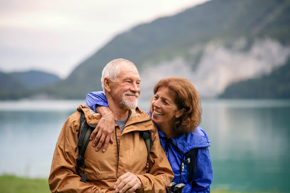 An older couple embracing on a hike beside a mountain lake, a picture of a healthy marriage investing in time away together